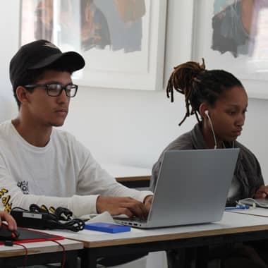 Young teenage boy and girl sitting beside each other working on laptops.